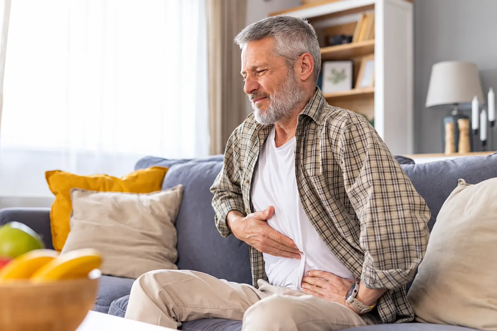 Man on the couch holding his stomach in discomfort