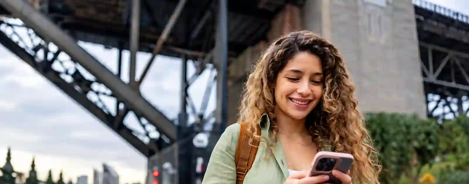 Woman smiling at her phone under the Sydney Harbour Bridge