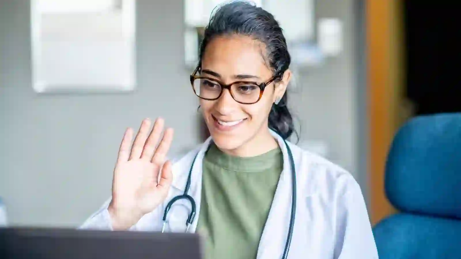 Doctor with a stethoscope waving hello during a video consultation
